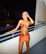 Vestido corto ajustado al cuerpo, con estampado abstracto en tonos naranja y marrón. Presenta escote asimétrico con abertura en el pecho y espalda descubierta.