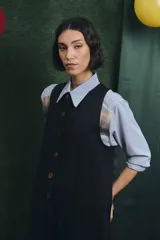 Mono largo de color negro con cierre frontal de botones vintage de distintos colores. Presenta un diseño sin mangas, con bolsillos laterales y una cinta para herramientas en la parte trasera.