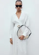 Vestido midi de lino color blanco, con cuello camisero, cierre frontal de botones, manga larga con puños abotonados y cinturón de tela con hebilla circular a tono.