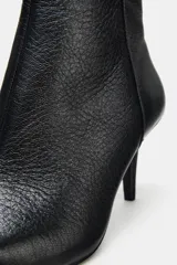 Botín de piel color negro con acabado texturizado, tacón fino medio y punta fina. Cuenta con cierre lateral mediante cremallera.