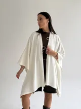 Ruana de tejido de punto trenzado en color crudo, con diseño abierto, corte holgado y mangas amplias tipo kimono.