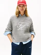 Sweater gris de tejido trenzado con cuello redondo y manga larga, confeccionado en algodón orgánico. Presenta un logo script TH gráfico bordado en color blanco en el centro del pecho.
