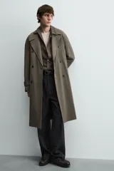 Trench color verde militar, de corte oversized, con cuello con solapas de muesca y manga larga con puño y trabilla. Presenta bolsillos de plastrón con solapa en la cadera y un bolsillo interior. Tiene una abertura en el centro de la espalda y cierre frontal de botonadura cruzada.