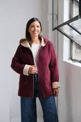 Tapado de paño bordó con interior en color beige, diseño con capucha, cierre frontal y bolsillos laterales. Presenta costuras visibles y puños vueltos que dejan ver el contraste de color.