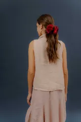 Chaleco de lino color marfil o beige claro, con diseño sin mangas, cuello alto amplio, cierre frontal con botones y bolsillos delanteros amplios. Presenta un corte asimétrico y relajado.