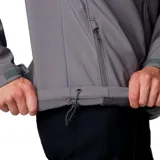 Chaqueta softshell Columbia para hombre, color gris, con cierre frontal, cuello alto, puños y dobladillo ajustables. Presenta bolsillos laterales y un bolsillo en el pecho, todos con cierre.