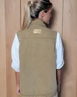Chaleco de gabardina color tostado, con cuello camisero, cierre frontal con botones metálicos y dos bolsillos frontales con solapa.
