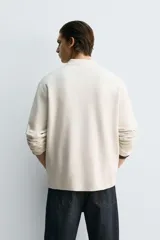 Polo de punto de manga larga con cuello solapa y cierre frontal de botones. Presenta un diseño de corte regular con aberturas laterales en el bajo.