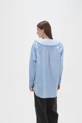 Camisa de algodón color celeste, con cuello grande tipo babero con volados, cierre frontal con botones y mangas largas con puños.
