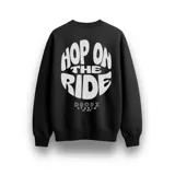 Buzo negro de algodón con interior suave y fit relajado. Presenta un estampado grande en la espalda con el texto "Hop On The Ride" en tipografía bold blanca y un diseño circular, debajo del cual se encuentra el logo "Dropz Studio Est. 2025".