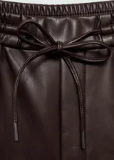 Pantalon tipo jogger de cuero sintético color marrón oscuro, con cintura elástica y cordón ajustable. Presenta un corte recto y diseño crop.