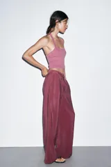 Pantalón de tiro alto color bordó, de corte ancho y pierna recta, con pinzas frontales y lazada ajustable en la cintura. El tejido presenta un acabado satinado o ligeramente arrugado.