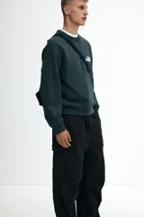 Pantalón cargo negro de algodón con corte holgado y tiro medio. Presenta cintura elástica con cordón ajustable, bolsillos laterales, bolsillos cargo con solapa y botón a presión en las piernas, y pliegues cosidos en las rodillas. El bajo es ajustable con cordón oculto.