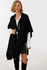 Ruana de punto color negro confeccionada artesanalmente en algodón, con diseño abierto y terminación de flecos largos en el ruedo. Incluye detalles de cuero integrados que aportan un estilo sofisticado.
