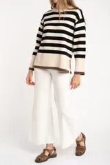 Sweater de punto a rayas horizontales negras y crudas, con cuello redondo y mangas largas. Tiene ribete marrón en puños y ruedo.