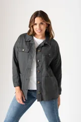 Campera de estilo camisa oversize en color gris oscuro, confeccionada en tejido de algodón con elastano. Presenta cuello clásico, cierre frontal con botones, bolsillos frontales con solapa en el pecho y bolsillos laterales tipo parche. Posee mangas largas con puños abotonados y un corte holgado ideal para media estación.