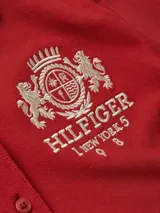 Chomba roja de algodón con elastano, corte slim, cuello polo y cartera de cuatro botones. Tiene un logo bordado en el pecho y la bandera de Tommy Hilfiger bordada en la manga.