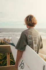 Remeron de algodón color verde musgo con efecto lavado, de manga corta y corte oversize. Presenta una estampa en la espalda con diseño inspirado en la playa, palmeras y flores, junto con la inscripción "Glassy Waves Club".