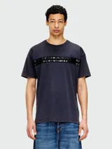 Remera de algodón color azul oscuro/negro con efecto lavado, cuello redondo y manga corta. Presenta una banda horizontal en el pecho con apliques negros brillantes y detalles troquelados.