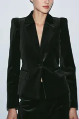 Blazer entallada de Zara Woman Collection confeccionada en tejido de terciopelo. Presenta cuello con solapas de muesca, manga larga con hombreras, bolsillos delanteros con solapa y cierre frontal con un botón. Incluye forro interior.