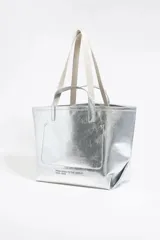 Bolso tipo tote de Bimba y Lola, color dorado con acabado metalizado y efecto arrugado. Presenta un diseño cuadrado con estampado central de la marca en un recuadro oscuro y doble asa de mano en color crema.