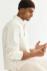 Remera polo de manga larga confeccionada en punto suave de algodón, con cuello inglés de sarga y tapeta con botones ocultos. Presenta hombros caídos, puños acanalados y aberturas laterales en el bajo, con un corte holgado.