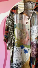 Camisa oversize de seda con estampado patchwork que combina diferentes patrones como cuadros, animal print, rayas y motivos florales. Tiene cuello camisero, botones frontales y mangas cortas.