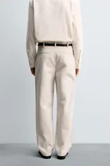 Pantalón de corte relajado confeccionado en tejido de algodón con estructura twill. Presenta pliegues frontales, bolsillos laterales y bolsillos traseros de doble vivo con botón. Cierre frontal con cremallera y botón.