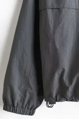 Campera rompevientos de nylon repelente al agua, con capucha ajustable, cierre frontal completo, bolsillos laterales y puños elásticos.