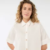 Camisa de corte holgado en color blanco, con cuello clásico, mangas cortas con dobladillo y cierre frontal con botones dorados en forma de estrella.