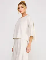 Blusa corta color beige de lino y viscosa, con escote redondo, mangas tres cuartos estilo kimono y corte holgado.