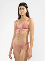 Conjunto de bikini color rosa con textura acanalada. El corpiño es de triángulo con tirantes finos y detalle de volados en el borde inferior. La bombacha es de corte clásico con tiras laterales ajustables.