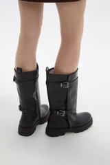 Bota de caña media en color negro, confeccionada en eco cuero con suela track dentada. Presenta un diseño con doble tira ajustable con hebillas metálicas en el lateral externo.