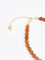 Collar de cuentas de vidrio color ámbar con un charm dorado en forma de llama en el centro. Incluye cadena de extensión y cierre de mosquetón.