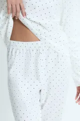 Pijama de dos piezas compuesto por remera de manga larga y pantalón, confeccionado en algodón blanco con estampado de lunares negros. La remera presenta cuello redondo y un pequeño bordado de corazones en el pecho.