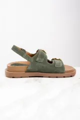 Sandalias de gamuza color verde militar con dos tiras anchas sobre el empeine y una tira trasera, todas ajustables con hebillas doradas. Suela plana color marrón.