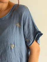 Blusa de manga corta color beige con delicados bordados florales dispersos, de corte holgado y escote redondo.