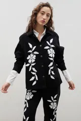 Camisa de denim negro con estampa floral blanca, cuello camisero, cierre frontal con botones y mangas largas.