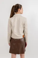 Campera estilo jeanera confeccionada en cuero ovino, con corte recto y largo a la cintura. Presenta cierre frontal con botones metálicos a presión, cuello clásico y dos bolsillos frontales con tapa.