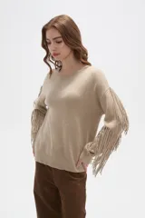 Sweater de punto color beige, con cuello redondo, corte holgado y diseño de flecos largos en las mangas.