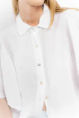 Camisa de lino color tostado, con cuello camisero y cierre frontal de botones. Se caracteriza por sus mangas cortas amplias y voluminosas que aportan un diseño fresco y liviano.