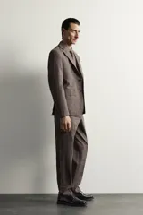 Blazer regular fit de Zara, confeccionada en tejido de lino y lana con diseño a cuadros en tonos marrones y grises. Cuenta con solapas de muesca, cierre frontal de un botón y bolsillos con solapa en la cadera.
