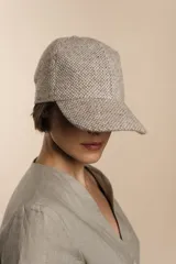 Gorra con visera confeccionada en lana fina sin teñir, con un sutil patrón de tejido en espiga.