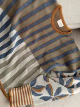 Sweater de tejido de punto con silueta oversize, cuello redondo y mangas largas abullonadas. Presenta un diseño patchwork con rayas verticales en tonos rojo, rosa y gris verdoso en el cuerpo, y un estampado floral en tonos rosa y rojo con detalles dorados en las mangas. Los puños y el cuello tienen un ribete a rayas horizontales.