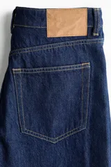 Jean de tiro alto confeccionado en denim de algodón lavado, con diseño de cinco bolsillos y piernas rectas de corte holgado. Cierre frontal con botón y cremallera.