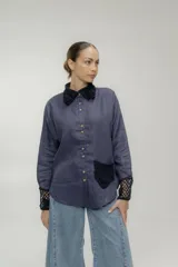 Camisa azul de lino con cuello clásico, cierre frontal con botones, bolsillo de parche y puños con detalle de crochet negro.