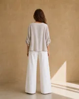 Blusa beige de lino de corte holgado y silueta oversize, con cuello redondo, cierre frontal de botones, bolsillos aplicados grandes y mangas tres cuartos con detalles de perforaciones bordadas en las mangas y el ruedo.