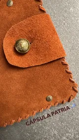 Set de accesorios compuesto por un sobre organizador de gamuza color marrón, un collar de cadena dorada, dos pares de caravanas colgantes y un prendedor, todos en metal dorado.