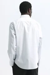 Camisa de vestir blanca con cuello inglés, tapeta clásica y corte ajustado. Presenta mangas largas con puños abotonados y bajo levemente redondeado.