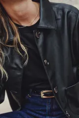 Campera corta negra de efecto cuero, con cuello camisero, cierre frontal de botones y dos bolsillos parche grandes en el frente.